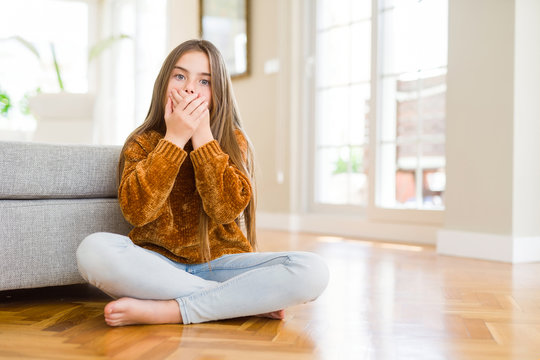 Beautiful young girl kid sitting on the floor at home shocked covering mouth with hands for mistake. Secret concept.