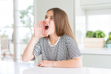 Beautiful young girl kid wearing stripes t-shirt shouting and screaming loud to side with hand on mouth. Communication concept.