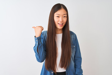 Young chinese woman wearing denim shirt standing over isolated white background smiling with happy face looking and pointing to the side with thumb up.