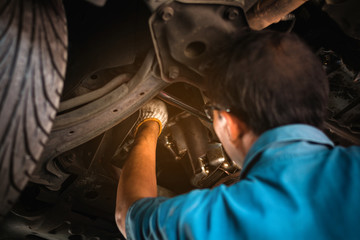 Mechanic repairing a car, Mechanic inspects car suspension system and chassis with a torch-lite under the car.