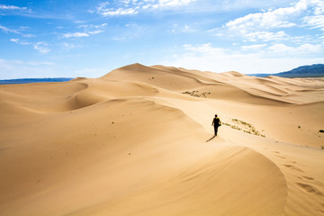 Woman walking in the mongolian desert sand dunes. Young woman walking golden sand on a bright summer day, Mongolia holliday vacation concept. - Powered by Adobe