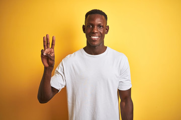 Young african american man wearing white t-shirt standing over isolated yellow background showing and pointing up with fingers number three while smiling confident and happy.