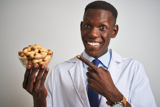 African american doctor man holding bowl with peanuts over isolated white background very happy pointing with hand and finger