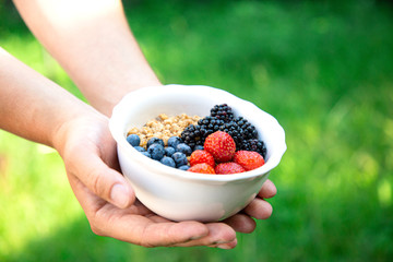 Man holding a bowl with crispy granola and fresh berries of strawberry, blueberry and blackberry. Natural organic meal. Green background. Healthy food concept.
