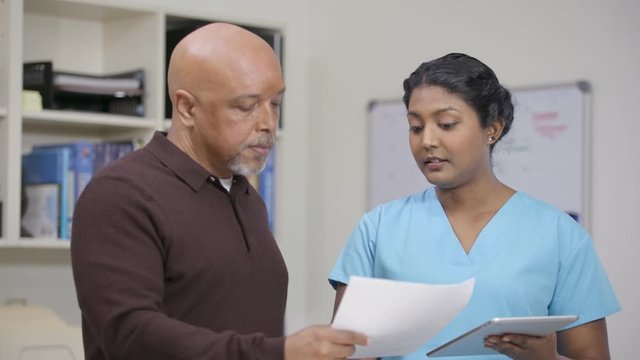 Nurse w/o stethoscope explains info on tablet and printout, slight camera move
