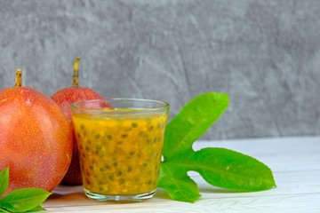 A glass of fresh passion fruits juice with green leaves and ripen passion fruits on white wooden table and concrete background.