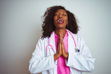 African american doctor woman wearing  pink stethoscope over isolated white background begging and praying with hands together with hope expression on face very emotional and worried. 