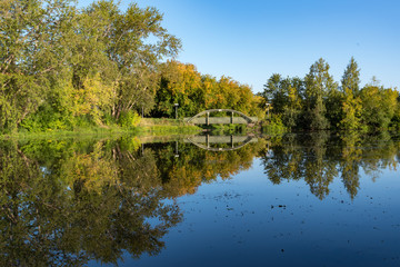 Fototapeta na wymiar Zakharyevsky park, a bridge across the Tabora pond, next to Tikhvin Assumption (Bogorodichny Uspensky) Monastery. Leningrad region. Russia