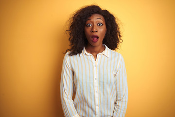African american woman wearing striped shirt standing over isolated yellow background afraid and...
