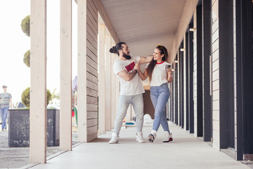 Positive young happy couple newlyweds dance synchronously walking around their hotel room in a tropical country during their holidays. Travel enjoyment concept