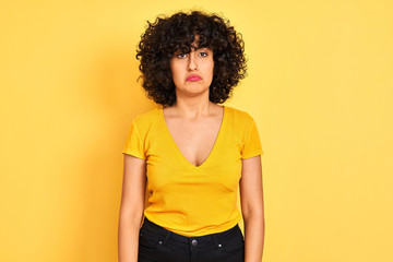 Young arab woman with curly hair wearing t-shirt standing over isolated yellow background depressed and worry for distress, crying angry and afraid. Sad expression.