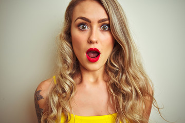 Young beautiful woman wearing yellow t-shirt standing over white isolated background scared in shock with a surprise face, afraid and excited with fear expression