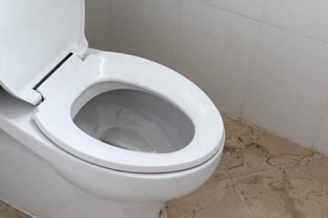 White toilet bowl in a bathroom with a dirty floor.