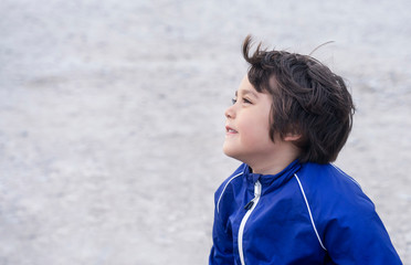 Side view portrait of cute little boy sitting alone with blurry sand beach background, Outdoor...