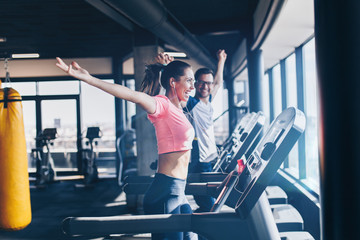 Young fit man and woman running on treadmill in modern fitness gym.