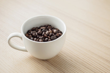 fresh roasted coffee beans in white cup on wood table
