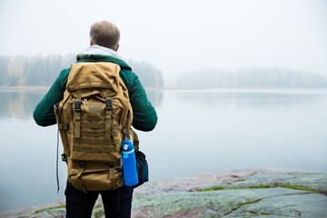 Mature man exploring Finland in the fall, looking into fog. Hiker with big backpack standing on...