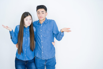 Beautiful young asian couple over white isolated background clueless and confused expression with...