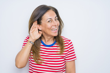Fototapeta premium Middle age senior woman standing over white isolated background smiling with hand over ear listening an hearing to rumor or gossip. Deafness concept.