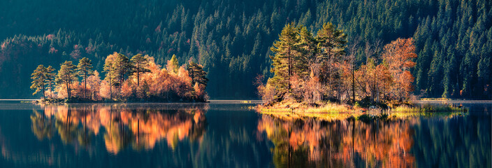 Panoramic autumn view of Eibsee lake. Unbelievable morning scene with first sunlight glowing small...