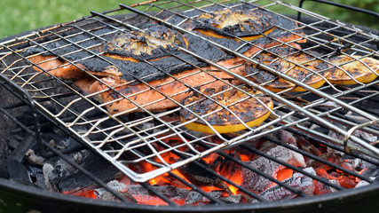 Grilling whole salmon fillets with gridiron. Fish and lemon slices are reaydy to eat. Skin is burned, but meat inside is ripe and juicy.