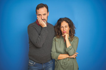 Beautiful middle age couple together standing over isolated blue background thinking looking tired and bored with depression problems with crossed arms.