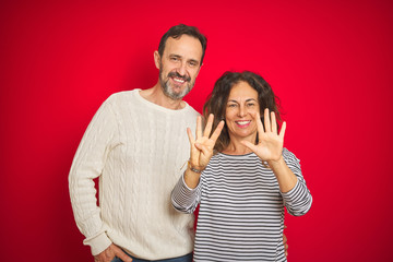 Beautiful middle age couple wearing winter sweater over isolated red background showing and pointing up with fingers number nine while smiling confident and happy.