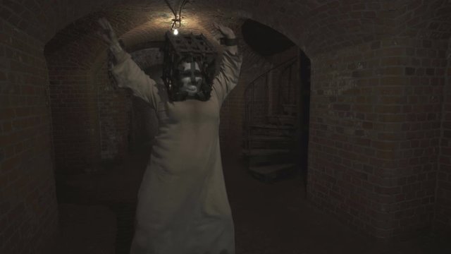 A funny ghost of a fat woman with a rusty cage on his head and with shackles on his hands dances in the gloomy corridor of old dungeon.