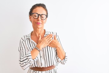 Middle age businesswoman wearing striped dress and glasses over isolated white background smiling with hands on chest with closed eyes and grateful gesture on face. Health concept.