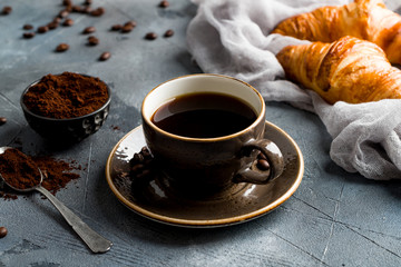 a Cup of coffee on the gray stone table with coffee powder and croissants