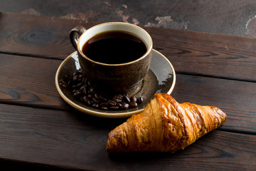 Cup of coffee with a croissant on a dark wooden tray