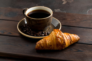 Cup of coffee with a croissant on a dark wooden tray