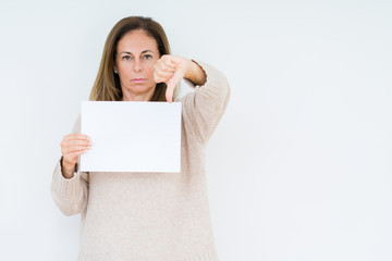 Fototapeta premium Middle age woman holding blank paper sheet over isolated background with angry face, negative sign showing dislike with thumbs down, rejection concept