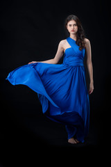 Cheerful young woman wearing blue dress standing and posing on isolates black background.Lady joyful and charming smile.