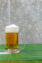 Mug of lager with foam on a green table with a concrete background