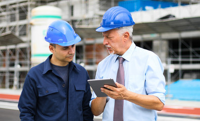 Fototapeta premium Two architect developers reviewing building plans at construction site using a tablet