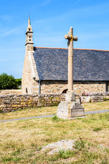 Side view of the granite chapel of Saint-Nicolas in Bugueles, Brittany, France, with its walled churchyard and calvary on the side of a small country road by a sunny summer day.