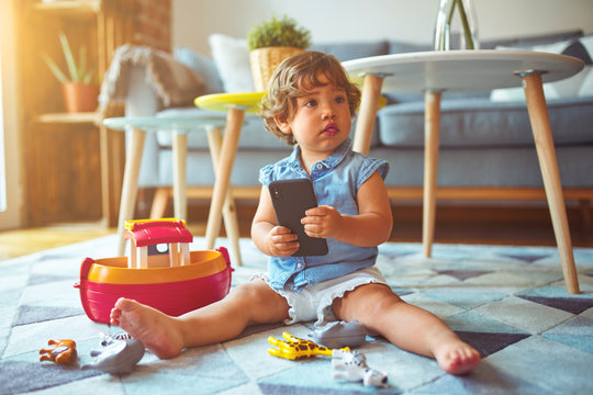 Beautiful toddler child girl sitting on the carpet playing with smartphone
