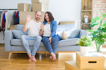 Fototapeta na wymiar Young couple sitting on the sofa arround cardboard boxes moving to a new house showing and pointing up with fingers number seven while smiling confident and happy.