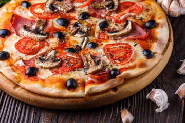 Pizza with tomato, olives, champignons, ham and cheese on round wooden plate