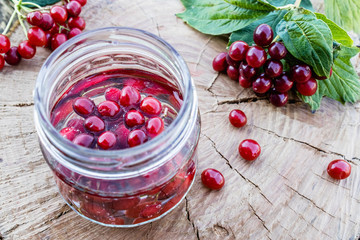 Jar with an elixir or tincture with viburnum berries on a wooden background, a red twig of viburnum in the background.