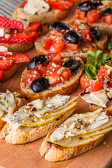 Assorted bruschetta with tomato, olives, camembert, blue cheese, lettuce, pear, honey on wooden board