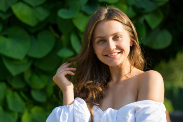 Young beautiful woman with bare shoulders in white clothes in the garden