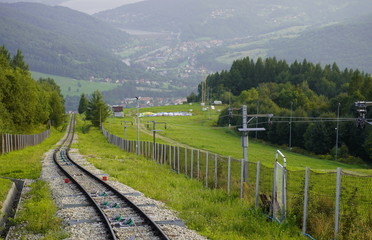 railway for the trailer in the mountains at the fence, the mountains in the summer in the grass and forests, at the foot of the house and the lake. transport links for transportation of people