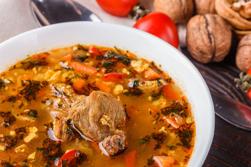 Georgian soup. Kharcho with rice, tomato, beef, garlic and herbs in bowl on wooden table