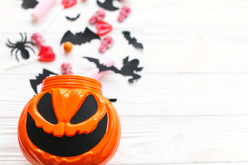 Trick or treat. Halloween candy spilled from jack o lantern bucket with skulls, black bats, ghost, spider decorations on white wooden background. Halloween sweets. Copy space.