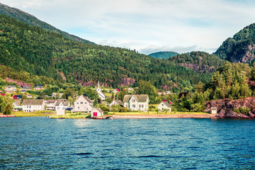 Fototapeta na wymiar Sunny summer view of typical Norwegian village on the shore of fjord. Beautiful morning scene of Norway, Europe. Traveling concept background. Instagram filter toned.