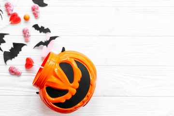 Trick or treat. Halloween candy spilled from jack o lantern bucket with skulls, black bats, ghost, spider decorations on white wooden background. Halloween sweets. Copy space.