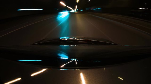 Car rides through city at night in a tunnel of neon lights, long exposure. Camera is mounted on roof of automobile. Reflection of light rays in windshield of auto. Theme a quick drive and night life.