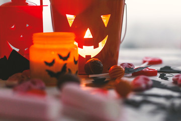 Halloween jack o lantern bucket, glowing candle, festive candy, skulls, black bats, ghost, spider decorations on white wooden background. Copy space. Trick or treat